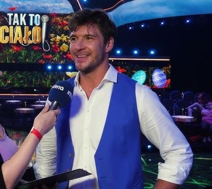 Mikołaj Roznerski w trakcie występu na planie filmowym lub teatralnym, ukazujący jego aktorski talent i charyzmę.