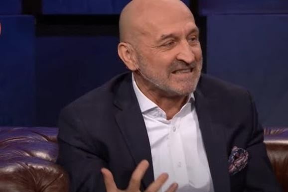 Kazimierz Marcinkiewicz podczas pracy, otoczony elementami nawiązującymi do jego kariery politycznej i zawodowej.