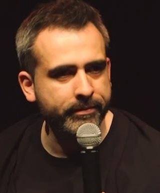 Abelard Giza podczas występu stand-upowego, trzymający mikrofon na scenie.